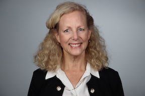 Portrait of a smiling woman with curly blonde hair in a black jacket and white blouse