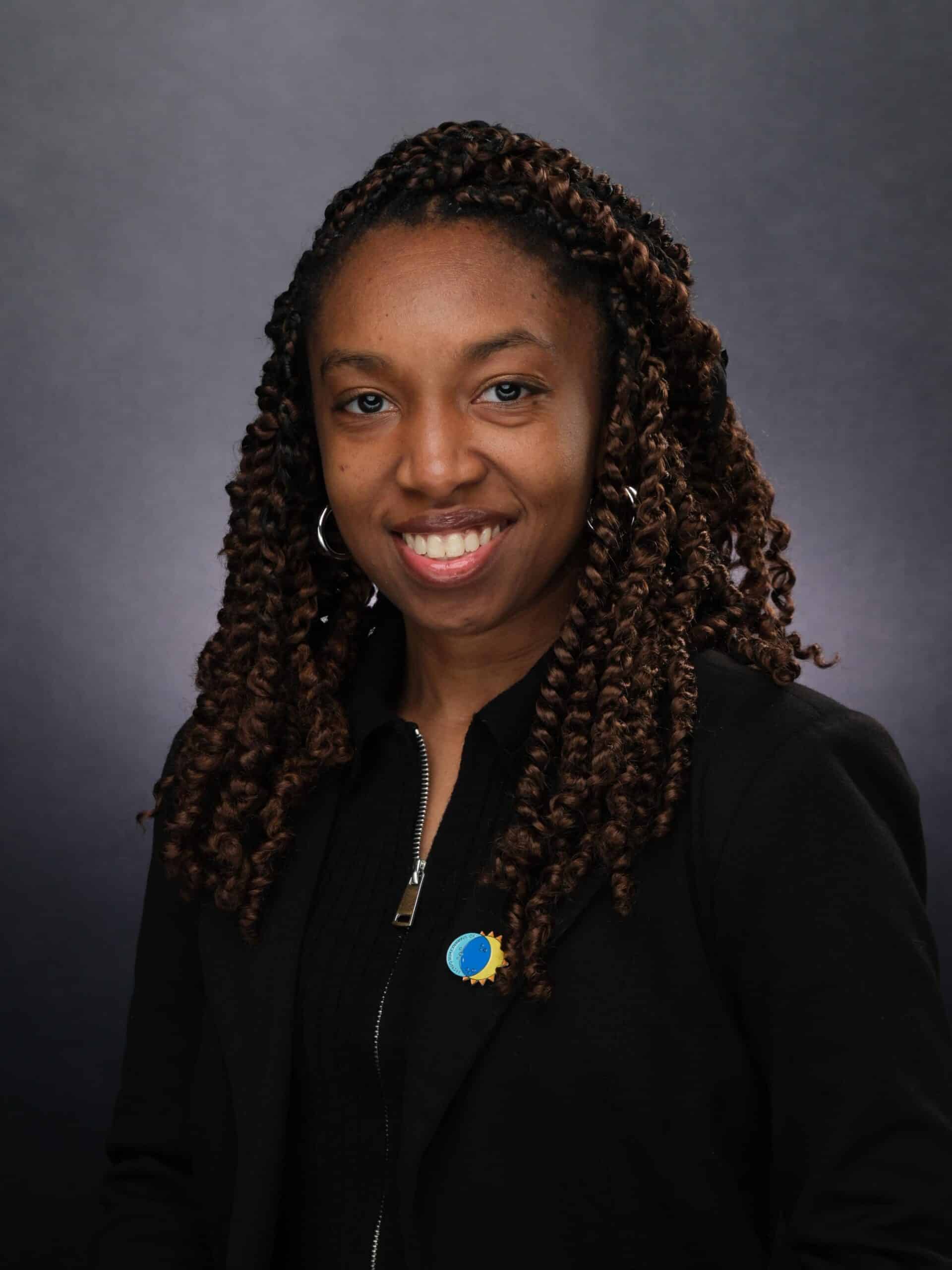 Portrait of a smiling woman with braided hair wearing a black jacket
