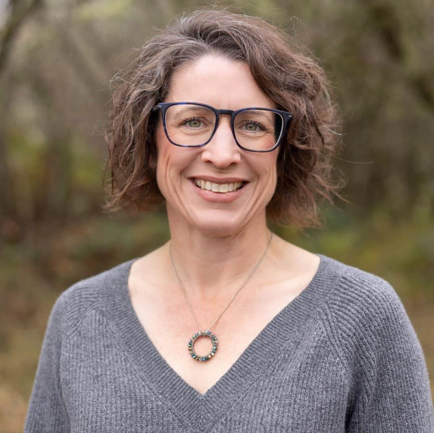 Portrait of a smiling woman wearing glasses and a gray sweater outdoors