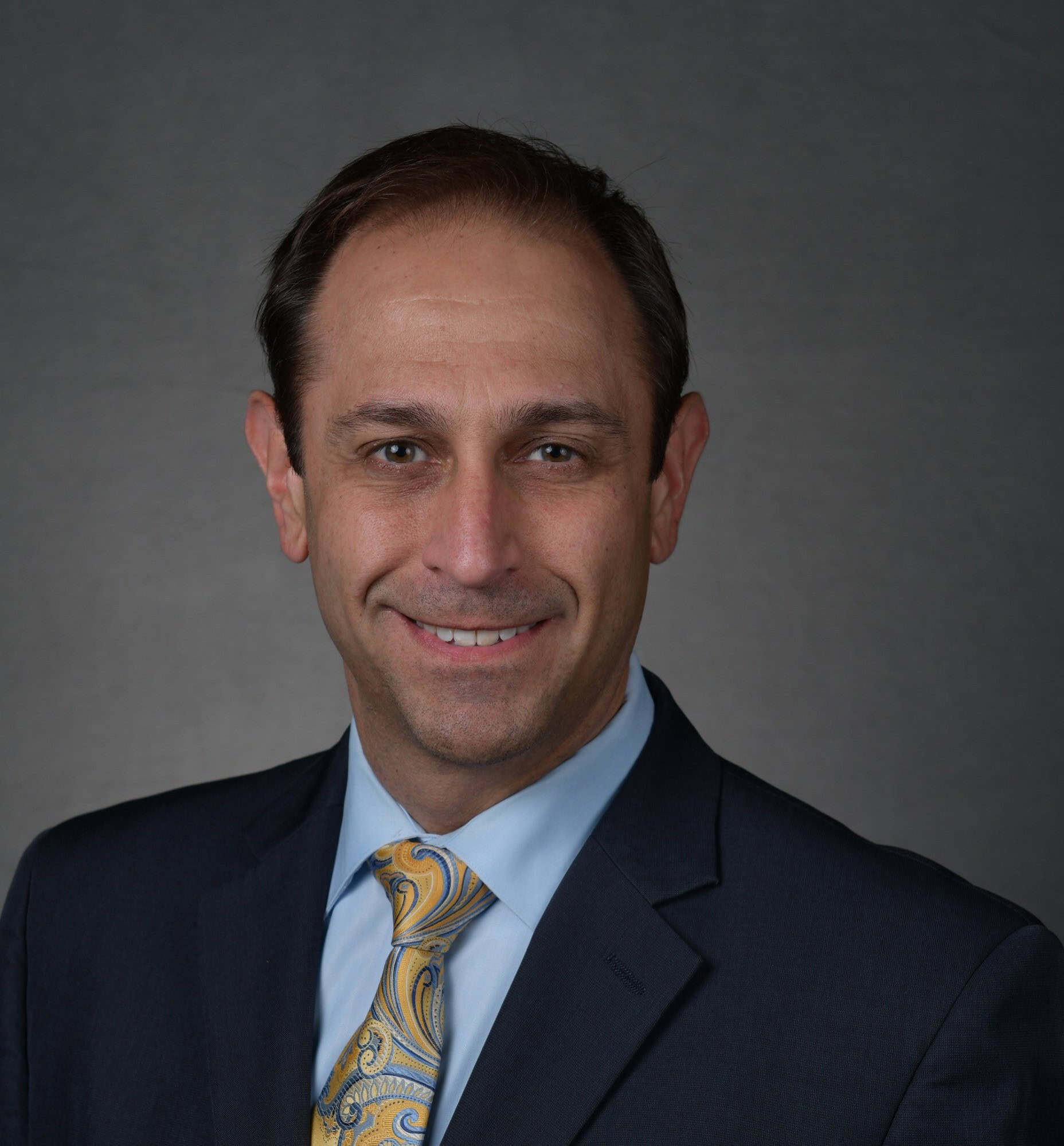 Portrait of a man in a suit and patterned tie against a gray background