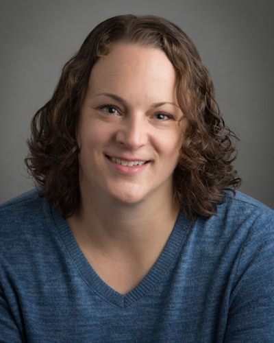 Portrait of a smiling woman in a blue sweater against a gray background
