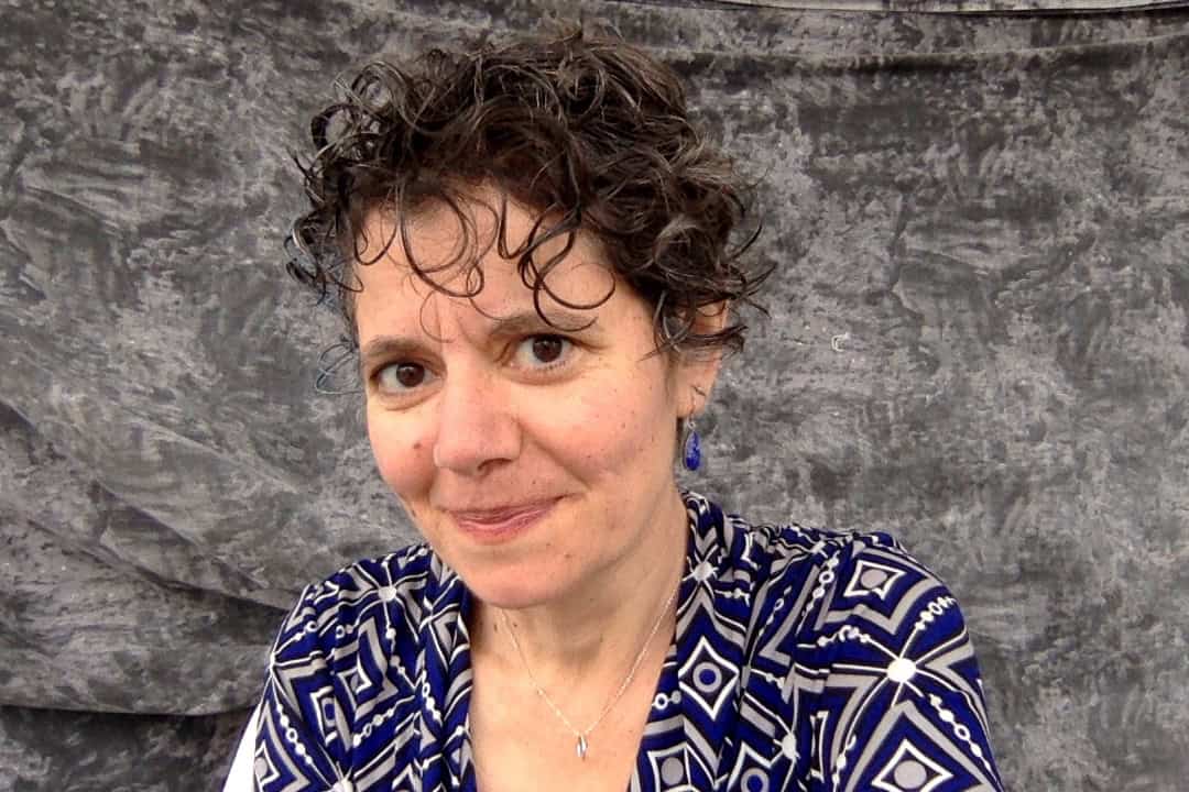 Portrait of a smiling woman with short curly hair in a patterned blue top against a gray backdrop