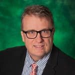 Headshot of a man wearing glasses and a suit against a green background