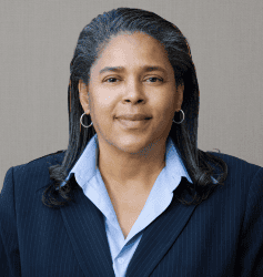 Portrait of a woman in a dark blazer and light blue shirt against a gray background