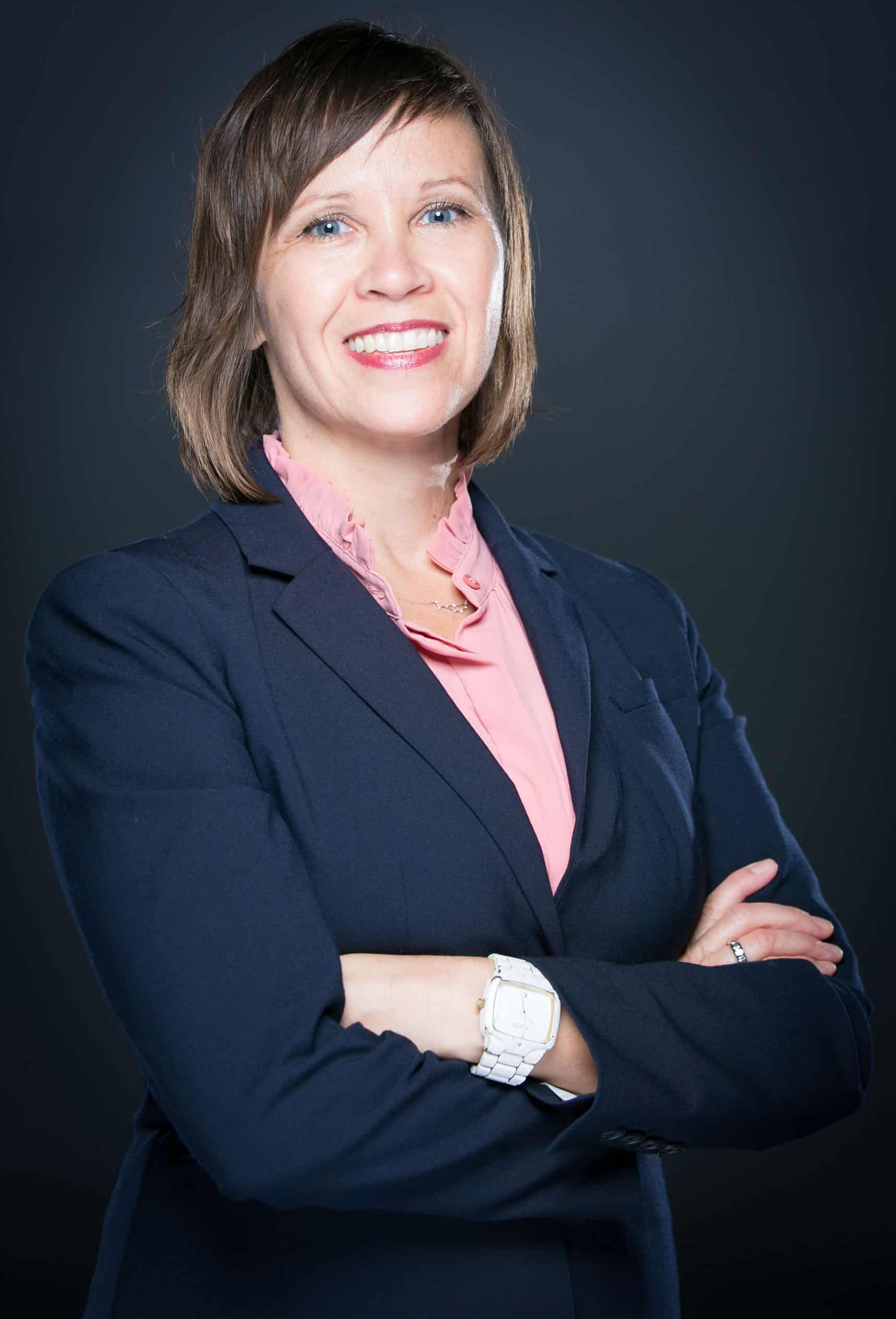 Portrait of a smiling woman in a navy blazer and pink blouse with her arms crossed