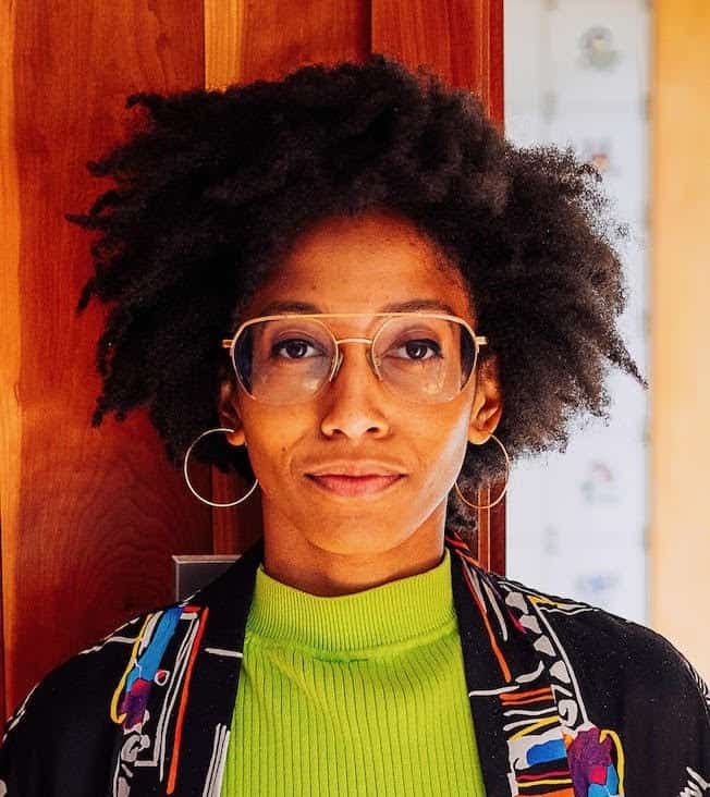 Portrait of a woman wearing glasses and hoop earrings, with natural hair and a bright green top
