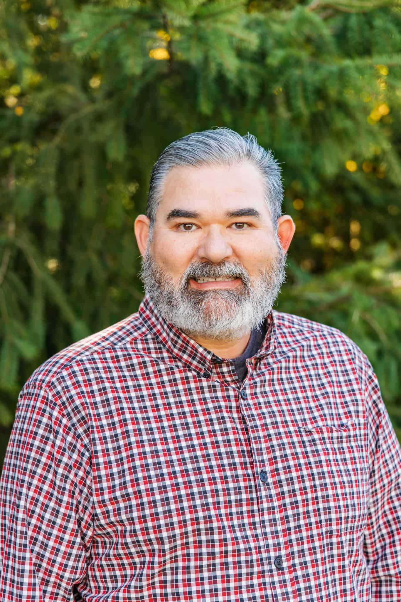 Portrait of a smiling bearded man in a red plaid shirt outdoors