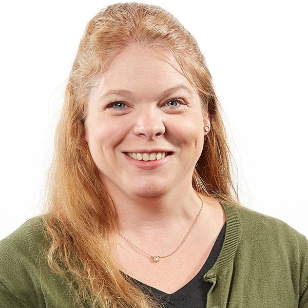 Portrait of a smiling woman with long blonde hair wearing a green cardigan and necklace