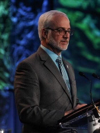 photo of Paul Kyle in a grey suit standing at a podium