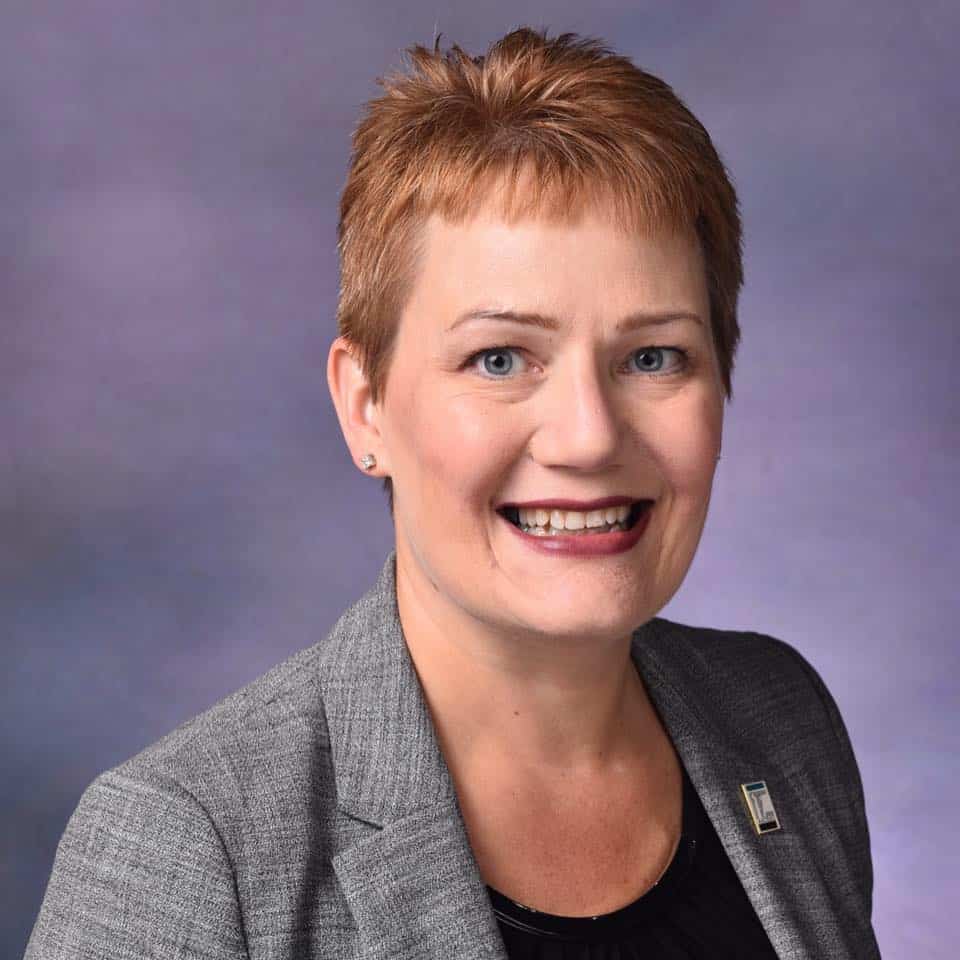 Portrait of a smiling woman in a gray blazer against a purple background