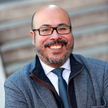 Portrait of a smiling bald man with glasses and a beard wearing a suit and tie