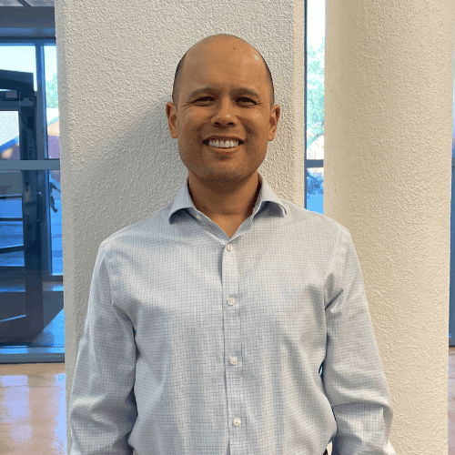 Smiling man in a light blue button-down shirt standing indoors