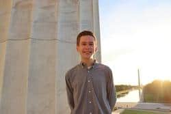 Young man standing beside a large stone monument at sunset