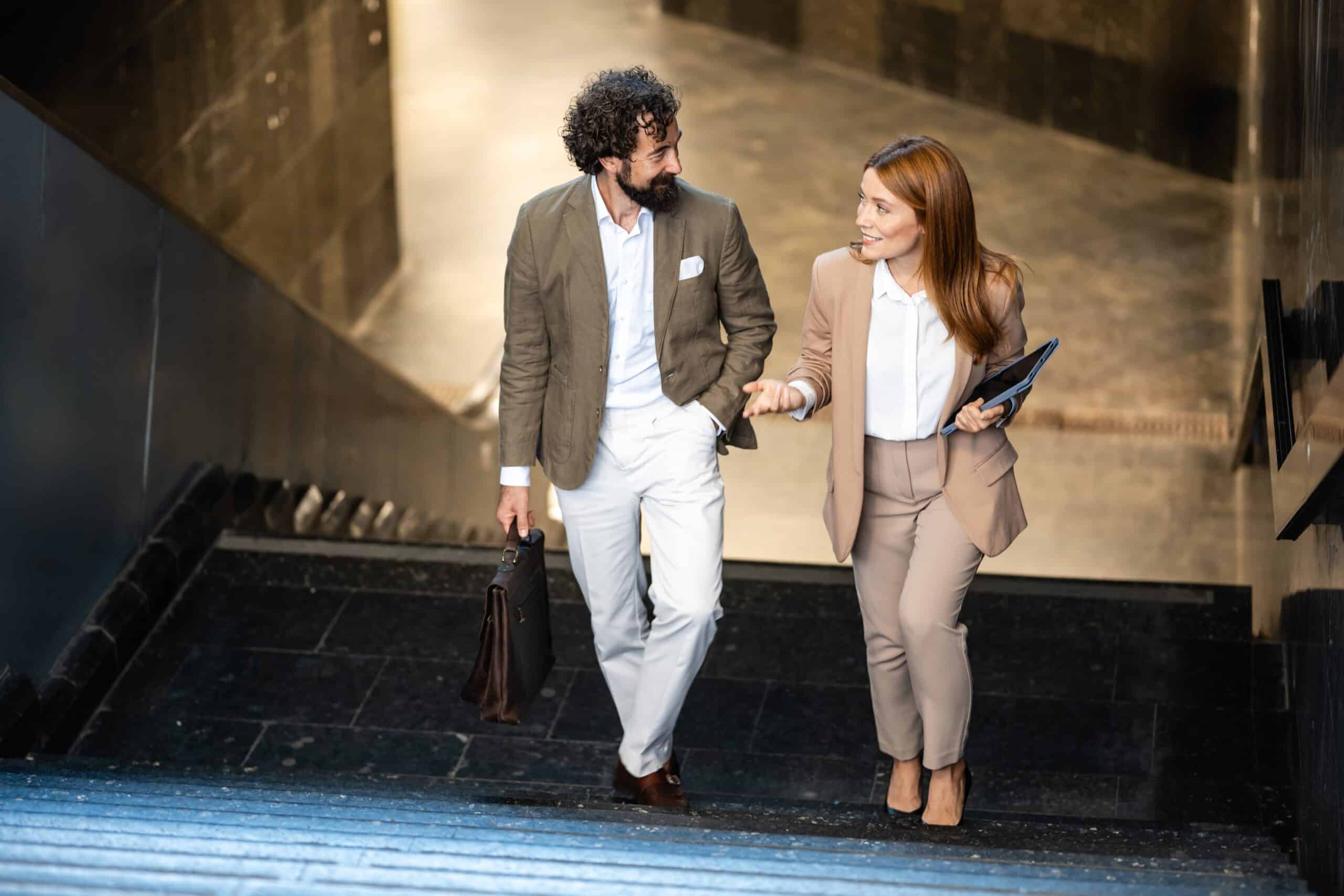 Business partners walking hand in hand to the stairs, engaging in conversations as they head to their offices, embodying teamwork and collaboration.
