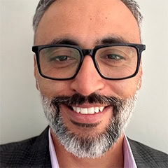 Close-up portrait of a smiling man wearing black glasses and a gray beard