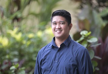 Portrait of a smiling man in a blue shirt outdoors with blurred greenery in the background