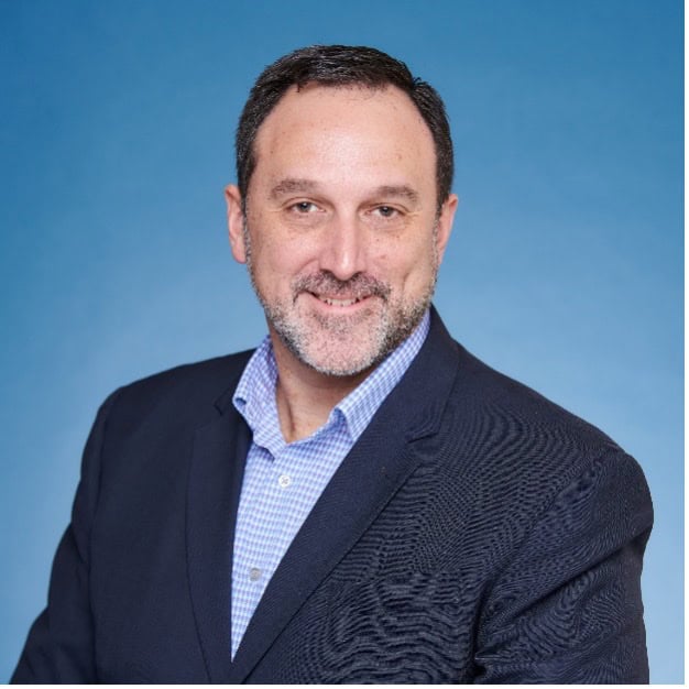 Portrait of a man in a dark blazer and blue checkered shirt against a blue background
