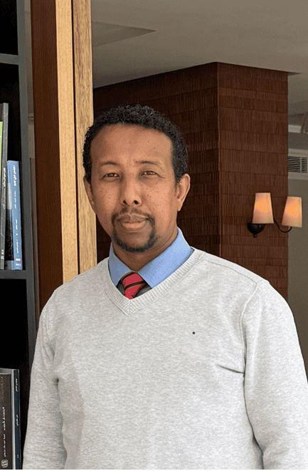Portrait of a man in a gray sweater, blue shirt, and red tie standing indoors