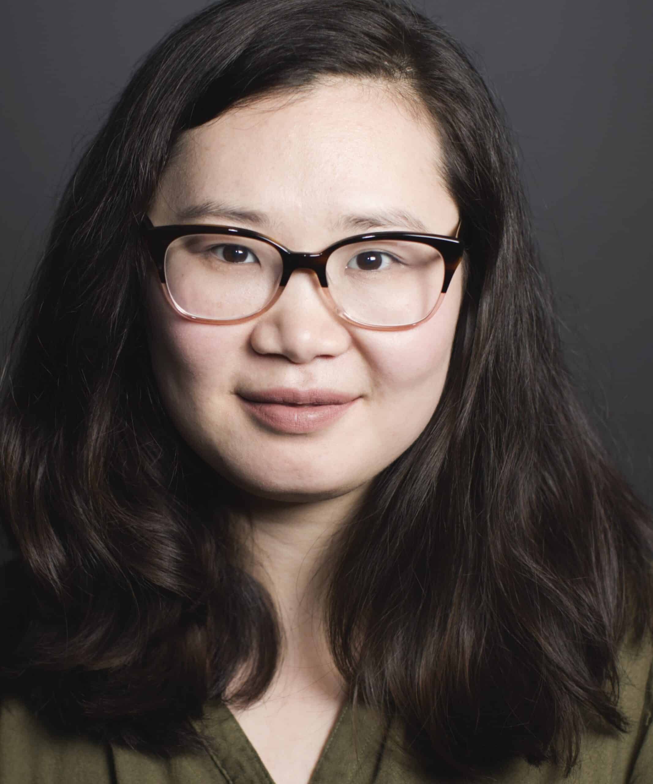 Portrait of a woman with long dark hair and glasses against a gray background