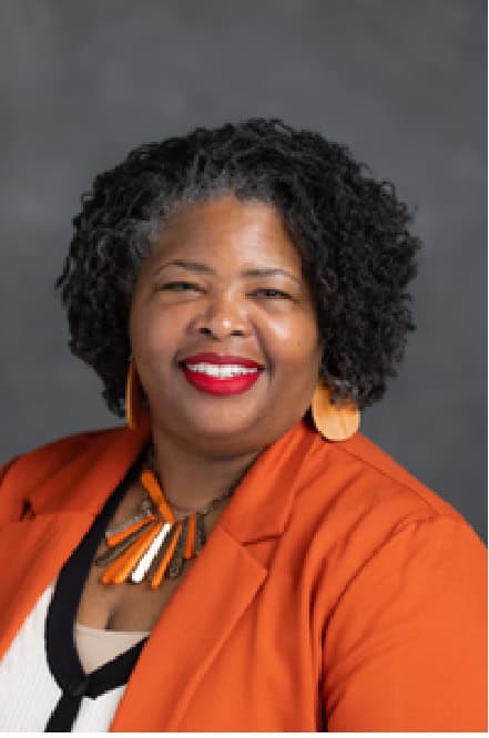 Portrait of a smiling woman in an orange blazer against a gray background