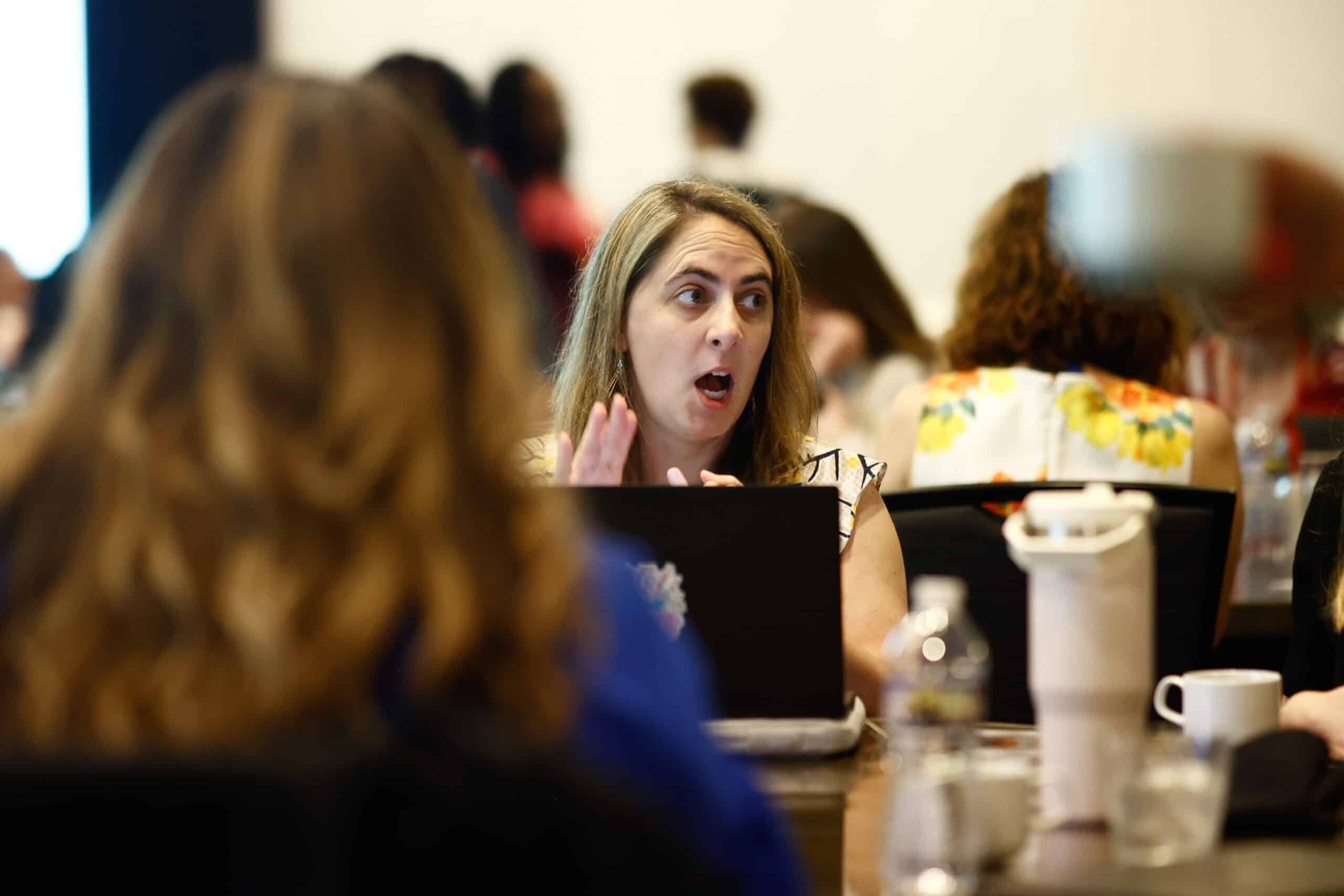 woman sitting at a working table with other people and talking in an AACRAO Event