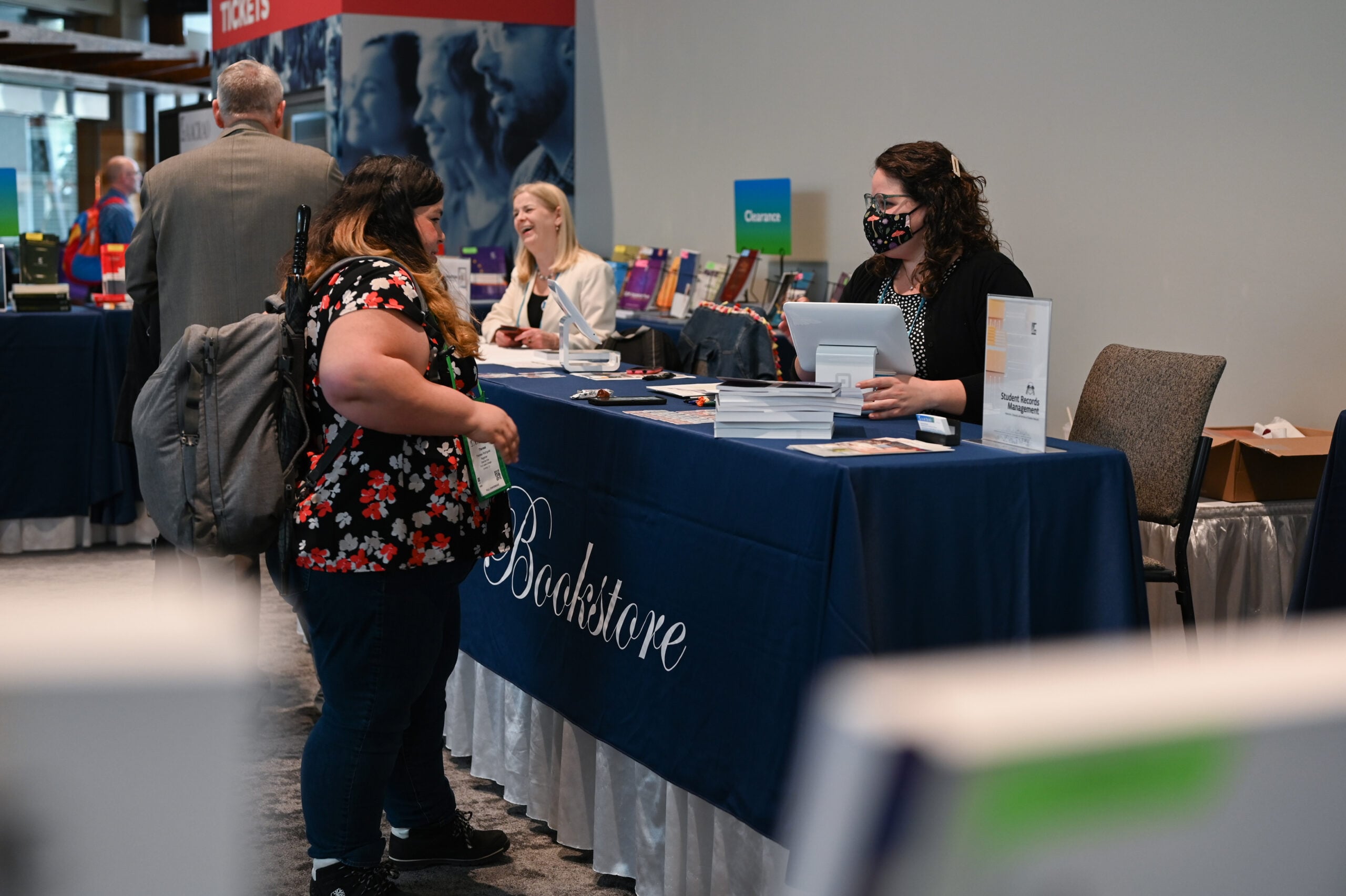 People talking at an AACRAO booth during a conference, with staff at a table handing out information