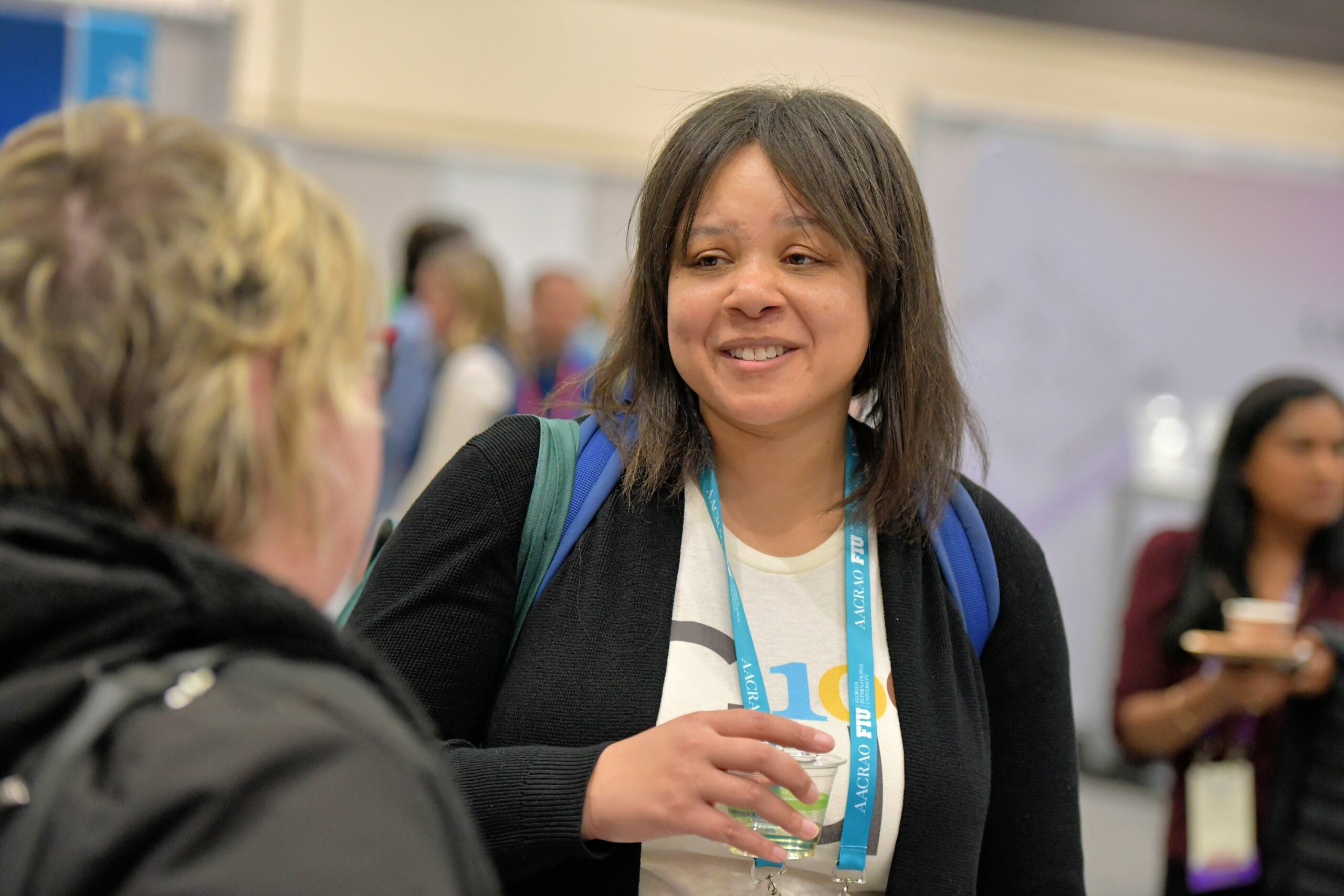 Woman smiling and speaking with attendees at an AACRAO event, holding a drink during a networking session