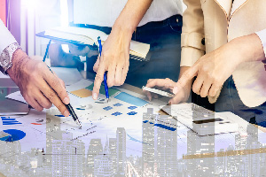 hands holding pens and pointing over a table with charts and data sheets