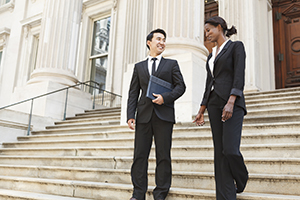 Two professionals dressed in suits walk side-by-side down a marble staircase.