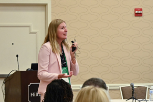session presenter in a pink blazer talking into mic