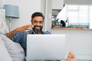 male smiles and talks with his hands on a video call while sitting on a couch