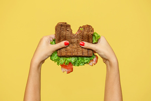 Hands holding BLT with bite taken out.