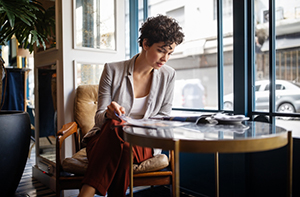 female in grey blazer sits at table near window and reads