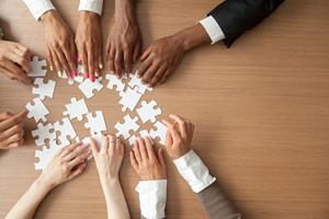 diverse hands from five people collaborate to put a puzzle together