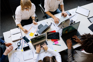 Group working around a table with computers, papers, notebooks.