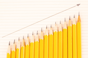A row of pencils on an upward slant with a graph line above showing the increasing height
