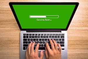 person typing on a laptop displaying a green screen with a progress bar at about 50%