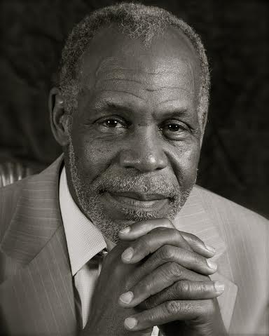 Portrait of an older man in a suit, resting his chin on clasped hands