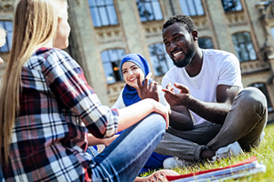 diverse group of students talk and laugh outside while sitting on grass