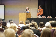 Photo from the audience's perspective of two speakers presenting from behind a podium.