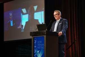 male speaker smiles from behind a podium at the 2019 AACRAO Annual Meeting