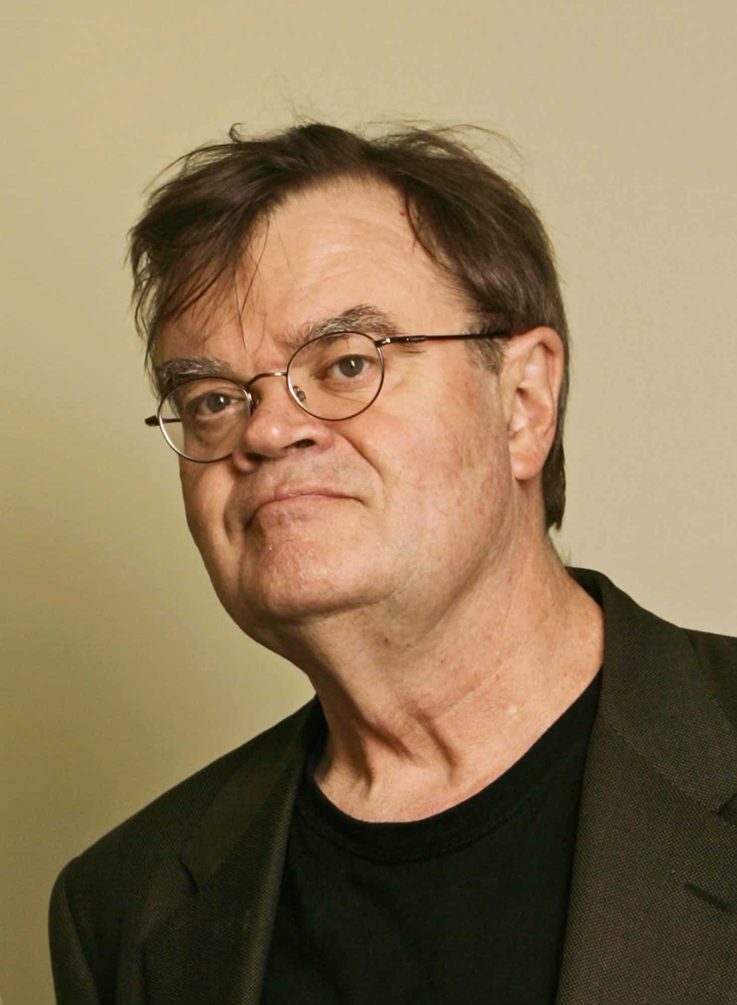 Portrait of a man wearing round glasses and a dark jacket against a plain background