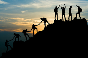 Silhouettes of hikers working together to get to the summit of a hill while the sun rises