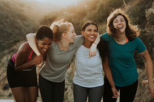 four females wearing active wear laugh with their arms around one another
