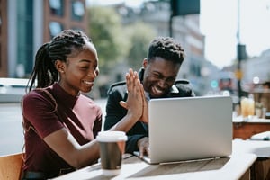 female and male of color high five and smile as they work over coffee