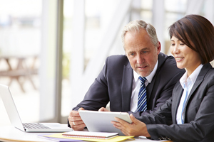 Two people dressed in business formal clothing review something on a tablet together