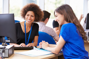 two females smile while looking at a computer together