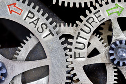 Interconnected gears with one turning to the left that says "past" and another turning to the right that says "future".
