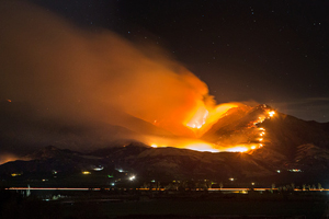 Photo of lava flowing down the side of a volcano at night with smoke filling the sky.