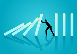 Cartoon figure stops a group of boxes from falling into a row of boxes lined up like dominoes.